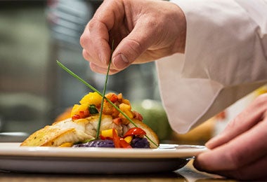Un primer plano de las manos de un chef colocando el cebollín final en un plato.