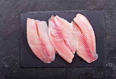 Filete de pescado blanco cortado por mitades sobre tabla de picar.