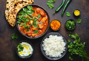 Plato de Butter Chicken con arroz basmati, naan y chutneys, sobre un fondo oscuro