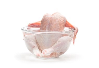 Carcasa de pollo cruda sumergida en un bowl de agua transparente, lista para cocinar un caldo de hueso de pollo casero