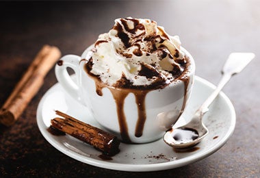 Chocolate caliente con crema batida, canela y chocolate en taza.