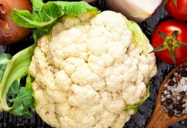 Coliflor entera y cruda junto a otras verduras.