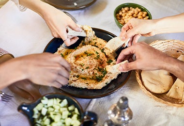 Amigos compartiendo hummus con pan pita, dos comidas mediterráneas.