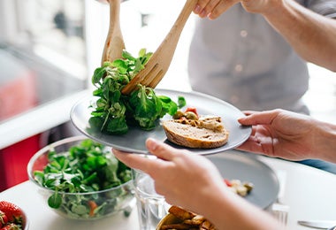  Una persona sirve una comida vegetariana con verduras y pan.