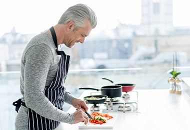 Hombre adulto feliz cocinando la cena en casa y sonriendo.