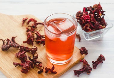 Vaso de agua de Jamaica con hielo con flores de Jamaica alrededor.
