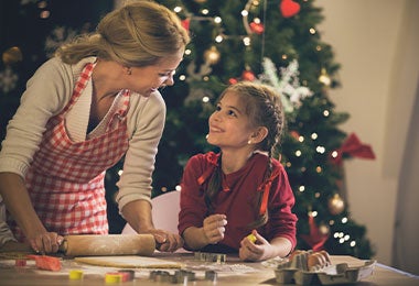 Madre e hija horneando galletas para Navidad, con arbol de navidad de fondo.