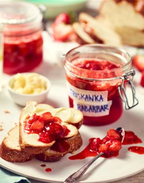 Mermelada de ruibarbo y fresas servida sobre tostadas con frascos en el fondo