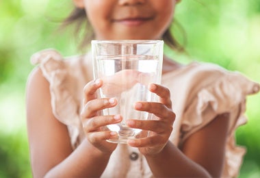 Niña sosteniendo un vaso de agua, un elemento vital para el buen descanso diario.