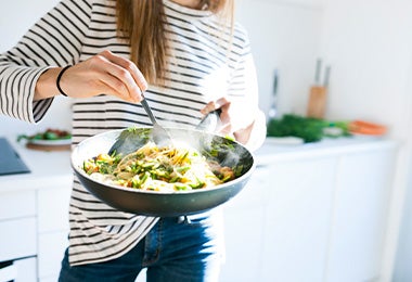 Una mujer salteando unos noodles con verduras.