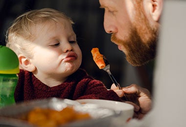 Padre alimentando a su pequeño hijo con sabrosa pasta. 