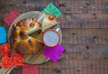 Pan de muerto cortado en pedazos con chocolate caliente.