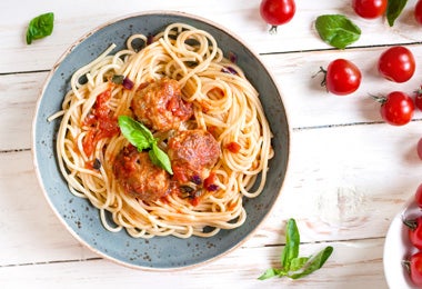 Plato de pasta a la boloñesa con tomates al lado para comer con bolillo.