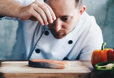 Chef sazonando un pescado antes de hacerlo en la freidora de aire.