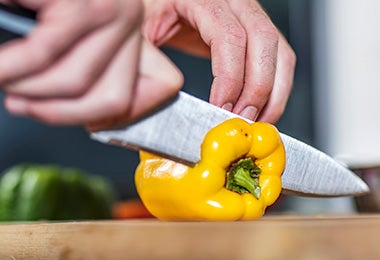 Un pimiento amarillo siendo cortado con un cuchillo.