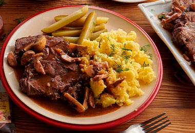Cabrito asado salteado con puré de papas servido en un plato junto con un sazonador Maggi