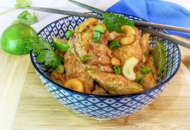 Bowl con pollo en salsa de marañones, decorado con cebolla fresca, cilantro y marañones enteros, acompañado de limón y palillos