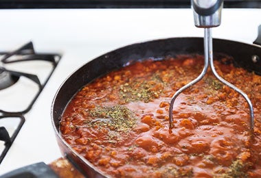 Salsa con hierbas italianas cocinándose en sartén sobre estufa blanca.