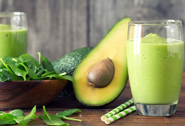 Smoothie de aguacate junto con aguacate tajado a la mitad.