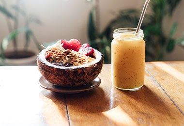 Smoothie de mandarina con maracuyá y un bowl de fruta servido en cáscara de coco.