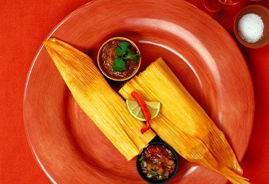 Tamales rellenos de pipián sobre plato rojo.