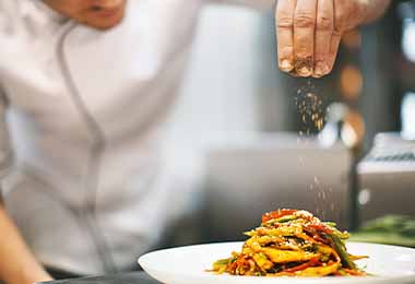 Un chef añadiendo condimentos y tipos de sales a un plato.