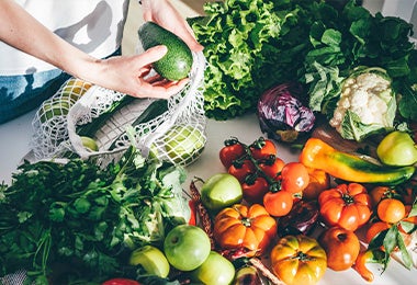 Verduras y frutas organizadas sobre un mesón blanco y una persona sacando otras de una malla blanca