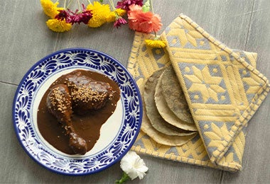 Dos piezas de pollo bañadas en mole Un plato con dos piezas de pollo bañadas en mole.