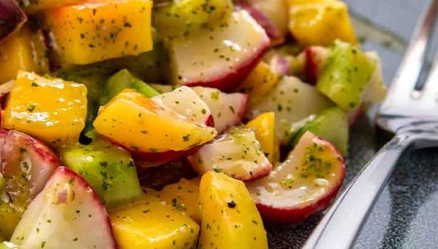 Una ensalada con mango y verduras, con su aderezo.