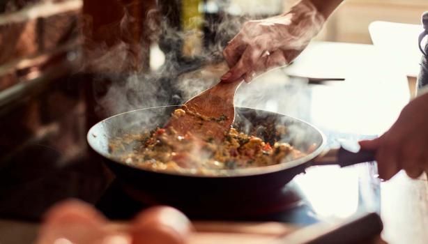 Una persona cocinando con una sartén y una espátula de madera. 