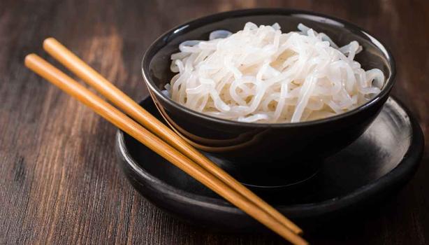  Noodles de arroz, servidos en un plato negro, junto a unos palillos chinos.