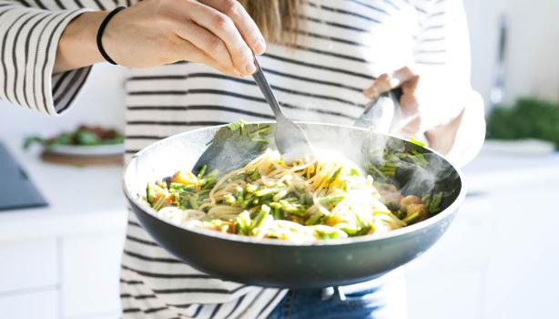 Una persona cocinando su comida con menos de 5 ingredientes en una sartén.