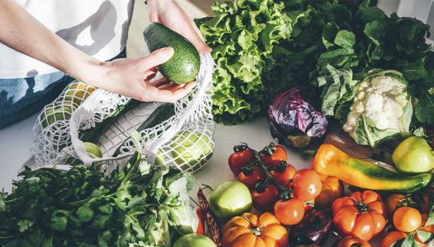 Una persona sacando productos orgánicos, frutas y verduras de una bolsa.
