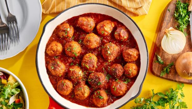 Albóndigas caseras en salsa putanesca servidas en una sartén con cebollas y cilantro