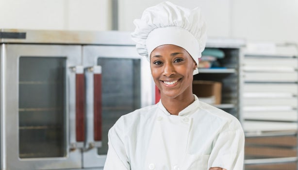 Una chef de pie con los brazos cruzados y vistiendo un uniforme.