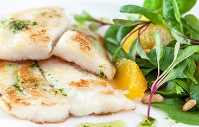 El pescado en freidora de aire se puede acompañar con ensalada. Pescado preparado en freidora de aire con una ensalada de hojas verdes.