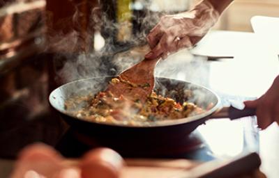 Tener artritis no significa que no puedas cocinar. Una persona cocinando con una sartén y una espátula de madera.