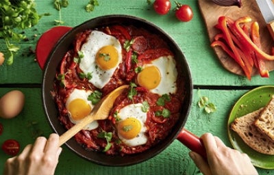 Huevos shakshuka con hierbas, salsa de tomate, pan y pimentón picado en toma cenital.