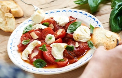 Ensalada caprese con tomate, queso, albahaca y pan en un plato.