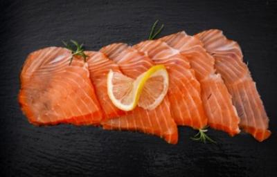 Salmón ahumando en frío, un delicioso manjar. Pequeños trozos de salmón ahumado frío sobre fondo negro.