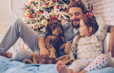 Padre y su adorable hija recostados en la cama con su perro. Al fondo, árbol de Navidad.