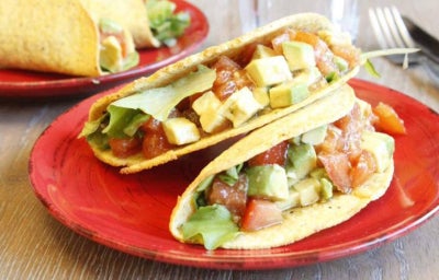 Dos tacos de ensalada de aguacate sobre plato rojo de cerámica para comer sin carne.