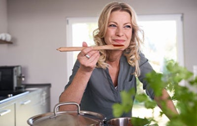 Mujer sonriente cocinando en la cocina probando salsa de tomate.