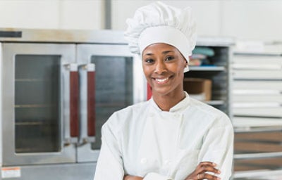 Una chef de pie con los brazos cruzados y vistiendo un uniforme.