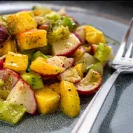 Una ensalada con mango y verduras, con su aderezo.
