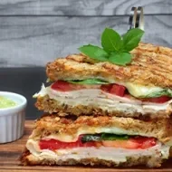 Pan panini relleno de jamón, tomate y albahaca, acompañado con salsa 