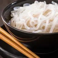  Noodles de arroz, servidos en un plato negro, junto a unos palillos chinos.