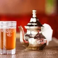 Bebida fermentada sin alcohol servida en una copa de vidrio y acompañada de una tetera de plata