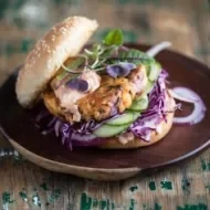 Apetitosa hamburguesa de pescado con vegetales emplatada y sobre una mesa de madera-