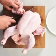 Corte de la carcasa de pollo sobre una tabla de madera, ideal para usar en caldos de hueso de pollo